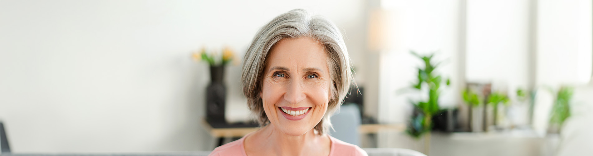 The image is a photograph of a woman with light skin, smiling at the camera. She appears to be in her late twenties or early thirties and has long hair. Her eyes are looking directly at the camera, and she is holding up her index finger near her mouth as if she s making a point or emphasizing something. The background is plain and light-colored, which suggests that this could be a stock photo used for various purposes such as advertising, personal branding, or lifestyle content.