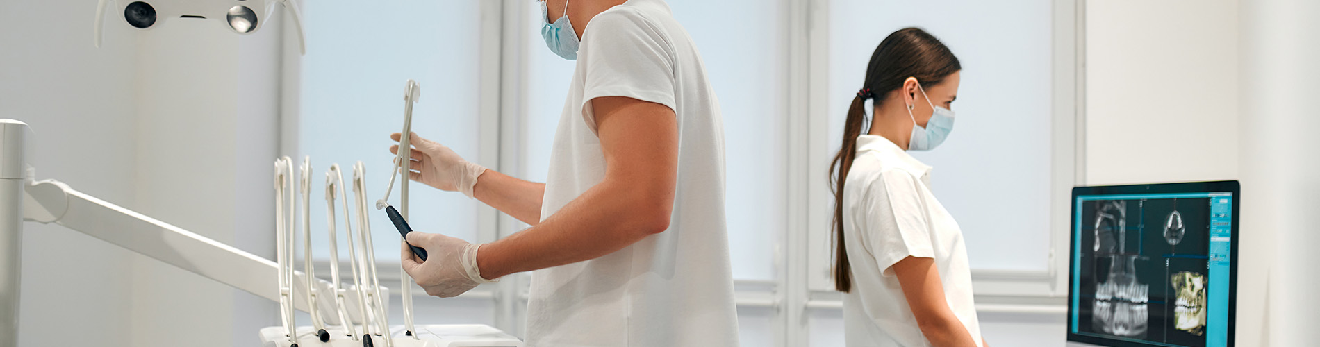 The image depicts a medical setting with two people dressed in white lab coats standing behind a counter, each holding a tablet device, with one person also operating a dental chair.
