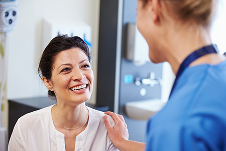 The image shows two individuals engaged in conversation one appears to be a woman with a white coat who could be a healthcare professional, standing next to another person who seems to be receiving attention or advice, possibly in a medical setting.