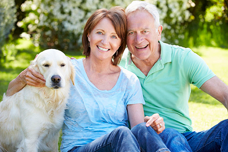 An elderly couple sitting on a bench with a golden retriever dog between them.