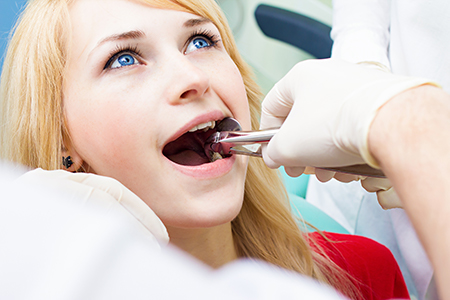 A woman receiving dental treatment with her mouth open, surrounded by medical professionals wearing gloves and using dental instruments.