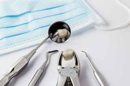 The image shows a dental office setting with various dental tools such as forceps, tweezers, and a toothbrush, along with a blue surgical mask and dental floss on a table.