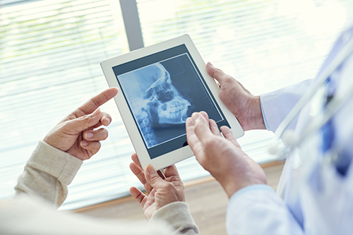 A medical professional shows a patient an X-ray on a tablet, with both holding the device in a modern healthcare setting.